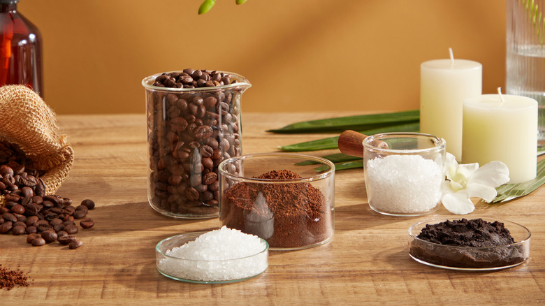 Glass containers of coffee beans, grounds, and coarse salt sit on a wooden table