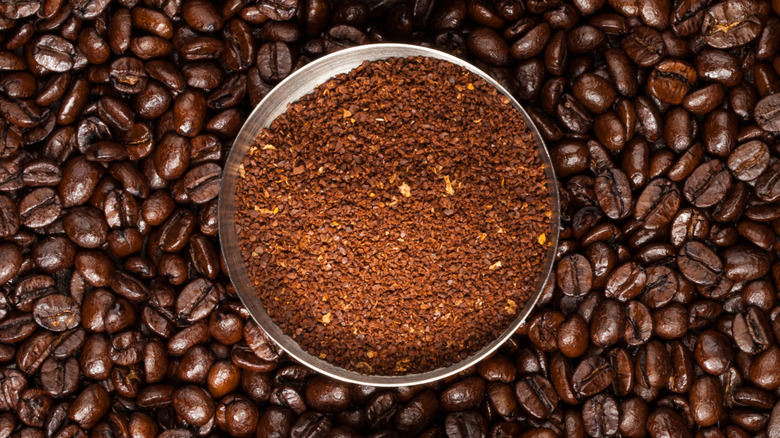A metal tin of coffee grounds sits on a layer of coffee beans