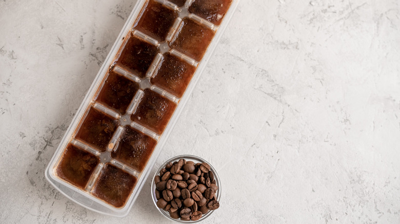 An ice tray of frozen coffee cubes sits next to a small bowl of coffee beans