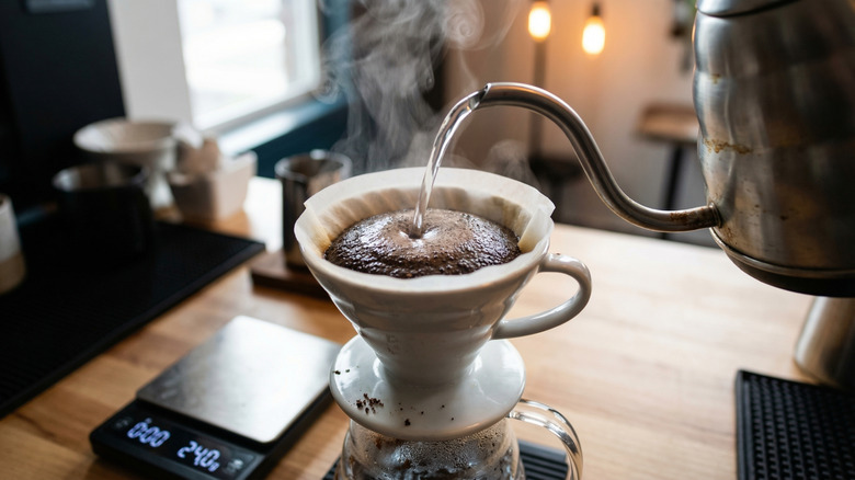 Water is poured from a metal pitcher into a ceramic pour-over coffee cup and filter