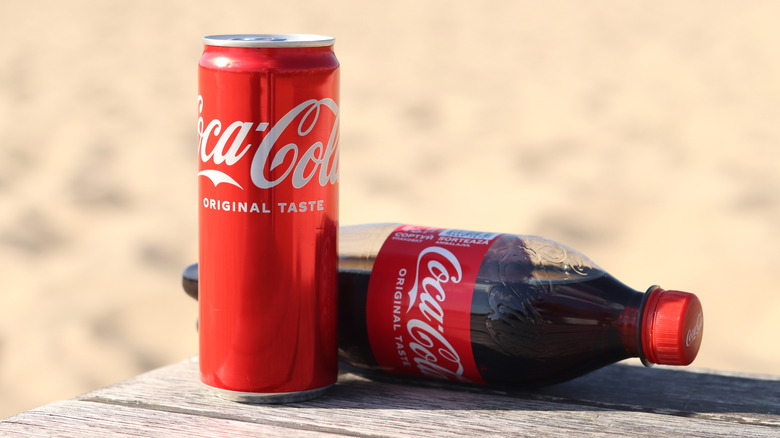A bottle and can of Coca-Cola Classic on a wooden table top