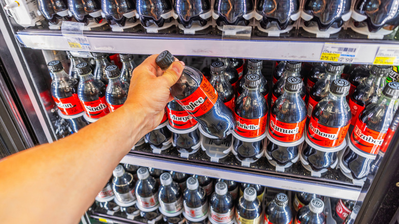 Hand reaching for Coke bottle from store fridge