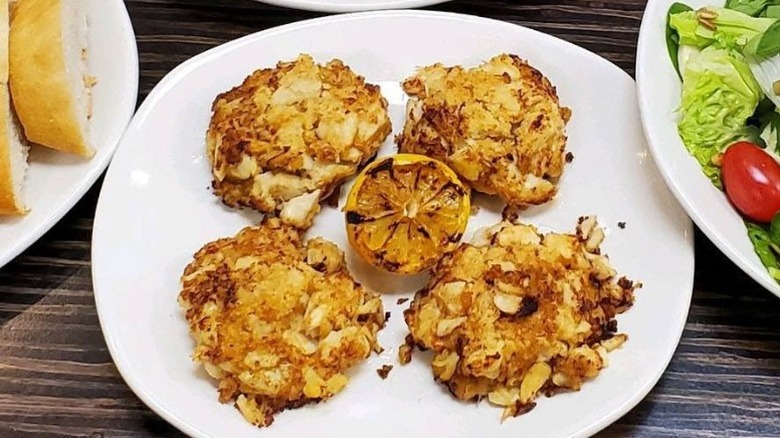 A plate of crab cakes with a grilled lemon on a white plate at Bonefish Grill