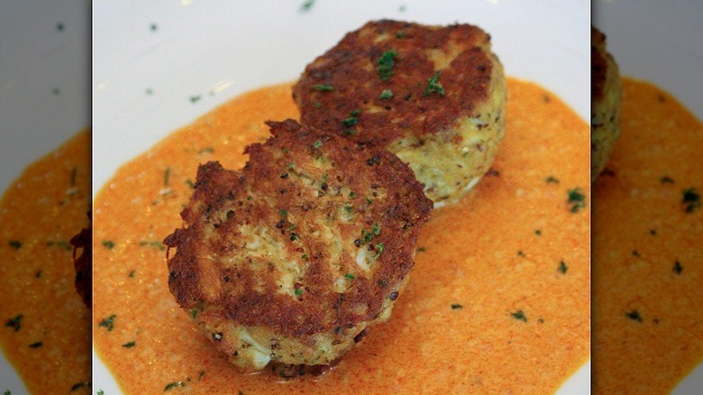 Two crab cakes rest in sauce on a white plate at Fleming's Prime Steakhouse & Wine Bar