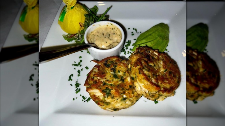 Two crab cakes and sauce sit on a white plate at Mastro's Steakhouse