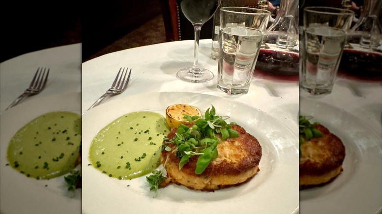 A crab cake and sauce sits on a white plate at The Capital Grille