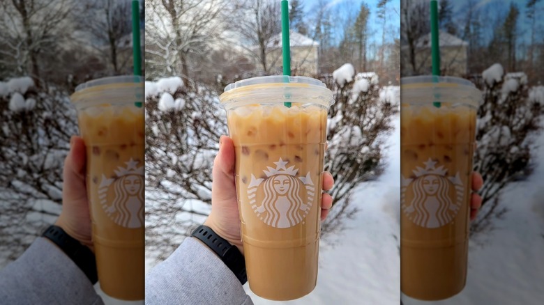 Hand holding Starbucks' Iced Blonde Vanilla Latte in front of a snow-covered landscape