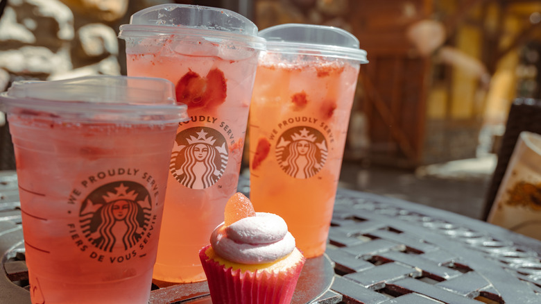 Three Strawberry Açaí Refreshers on a black table next to a cupcake