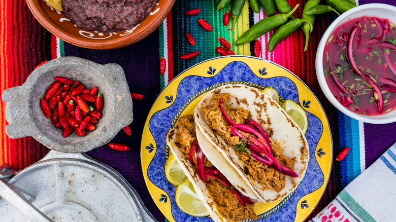 A colorful table with tacos, dried chillies and pickled onions