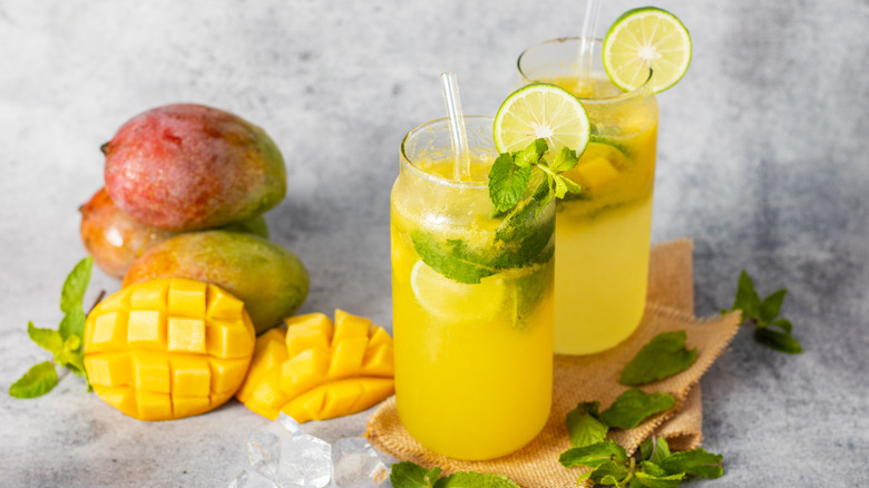Mangoes and glasses of mango soda with fresh lime and mint garnishes