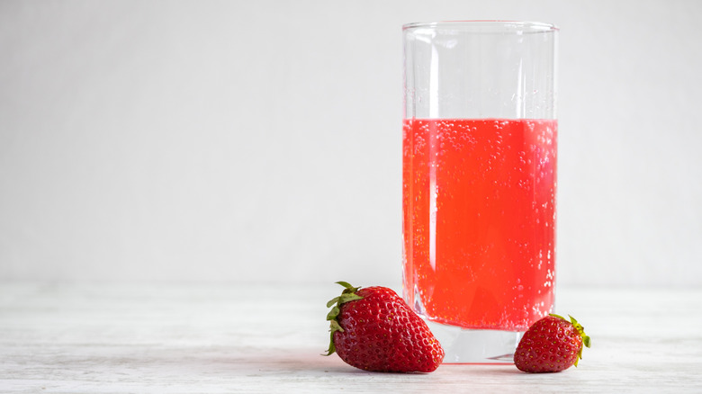 A glass of strawberry soda with a couple of fresh strawberries in front