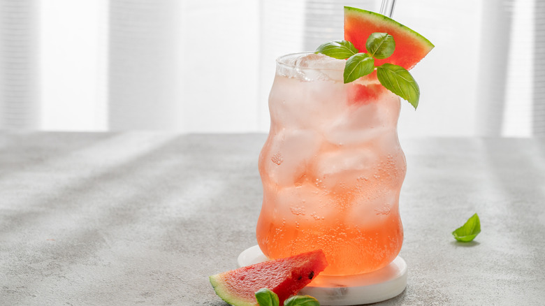 A glass of watermelon soda with fresh fruit and basil garnishes