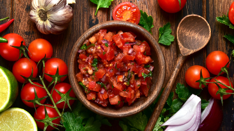 Wooden bowl of freshly made salsa with the ingredients used surrounding it