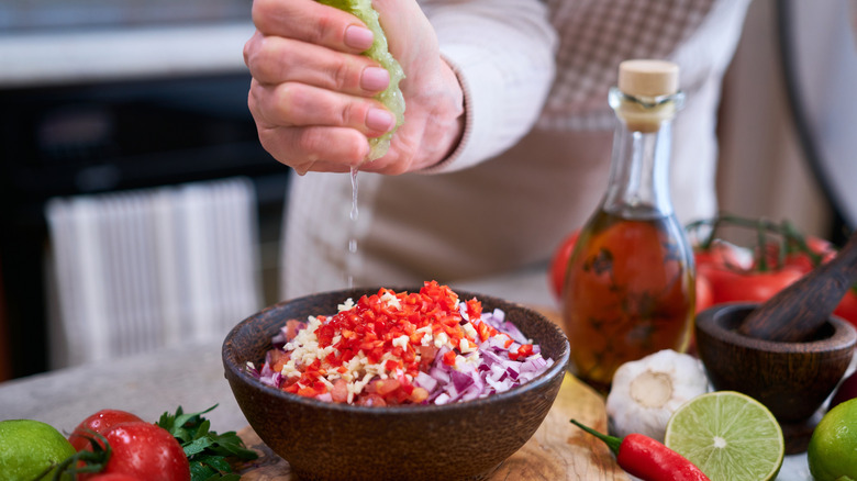 Hand squeezing lime juice into a bowl of chopped ingredients for salsa
