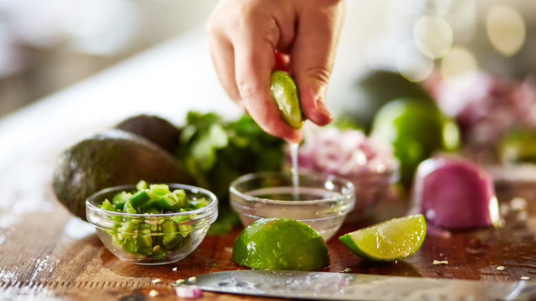 Hand squeezing lime juice into a bowl next to diced spicy peppers