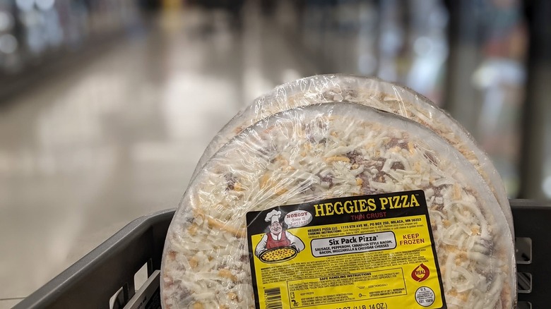 Two frozen Heggie's Six Pack pizzas sit upright in a grocery store shopping cart