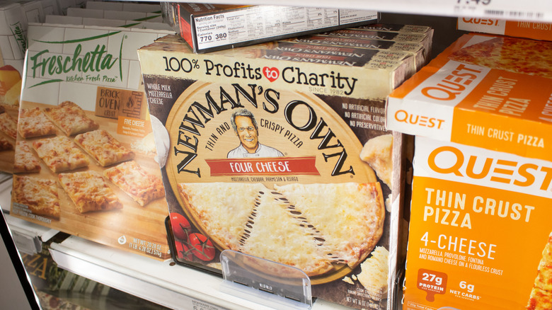 Store freezer shelves full of frozen pizzas, with Newman's Own Thin & Crispy Four Cheese Pizza prominently displayed in the center