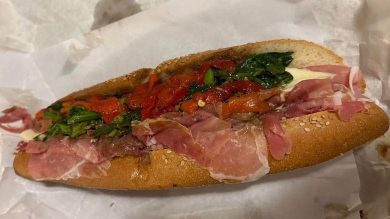 A long Italian sub on parchment with roasted peppers and spinach
