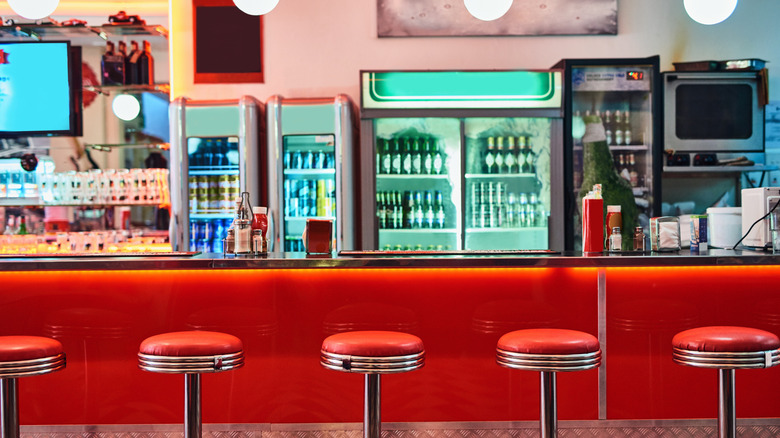 A red diner counter, red and chrome stools and several fridges behind the counter