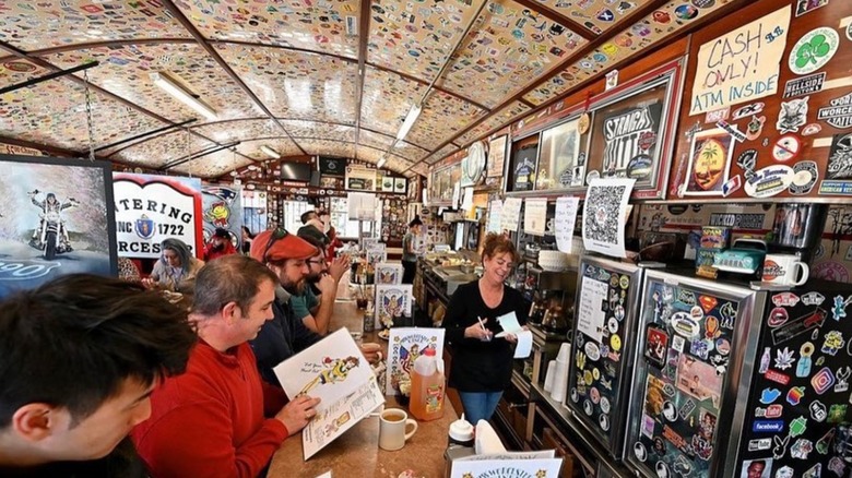 They busy interior of the diner with stickers all over the ceiling and lots of people at the counter