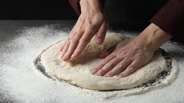 Person flattening out pizza dough with their hands