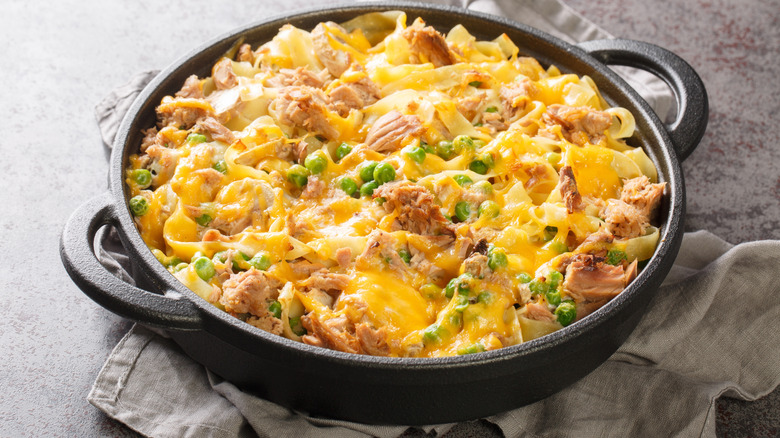 Cheesy pasta dish with tuna and green peas in black pan