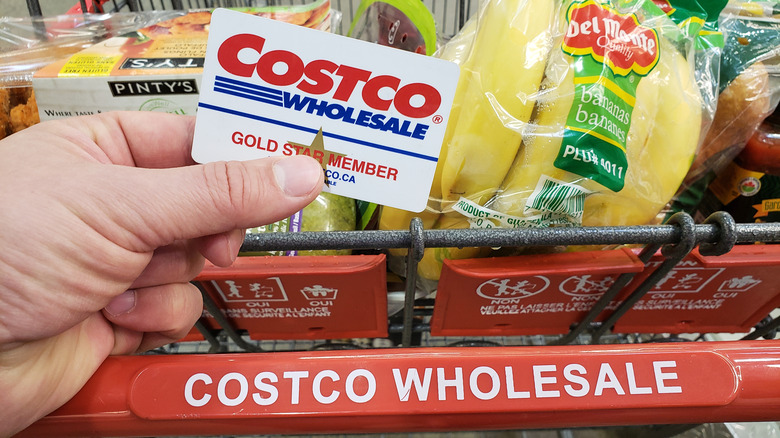 Person holding Costco member card in front of cart