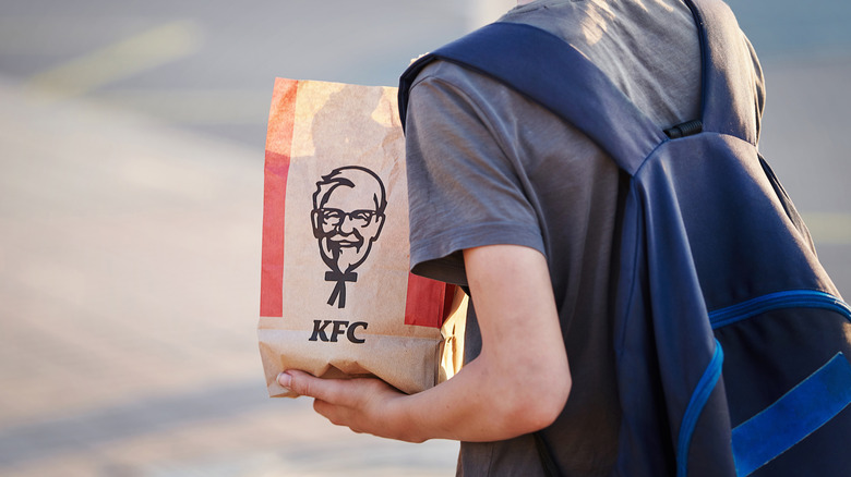 Kid with backpack carries KFC bag.
