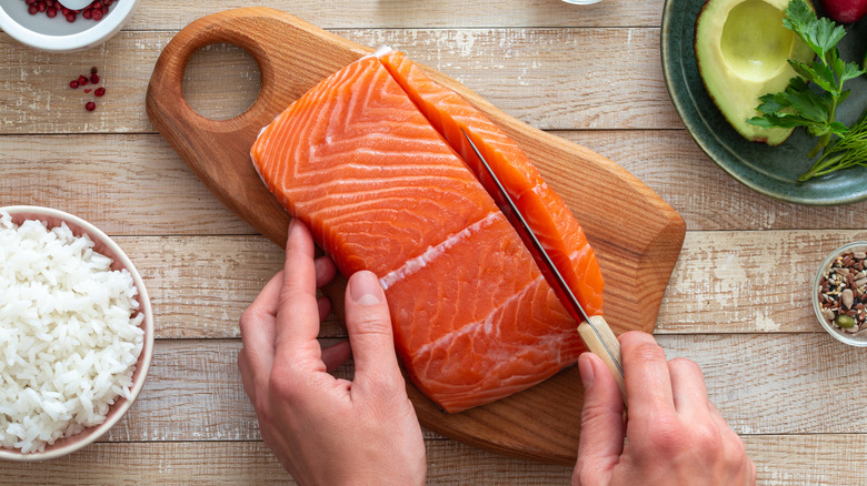 A chef cuts into a fillet of salmon that is sitting on a wood cutting board