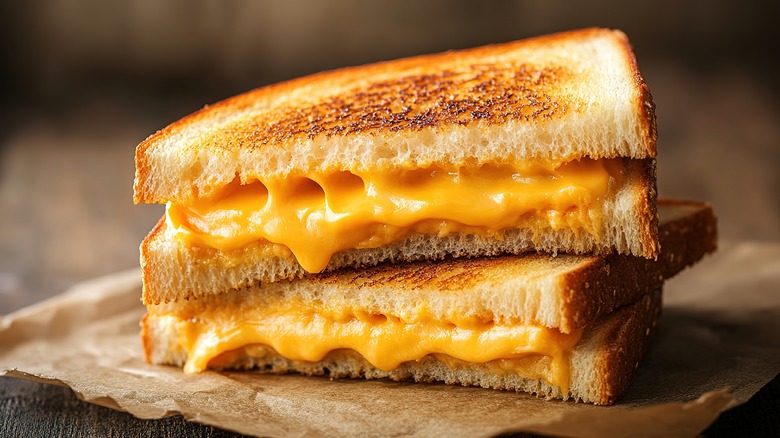 Grilled cheese sandwich halves stacked on parchment paper on a wood table.