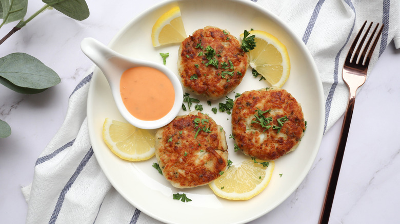 Crab cakes on a plate with remoulade, herbs, and lemon slices