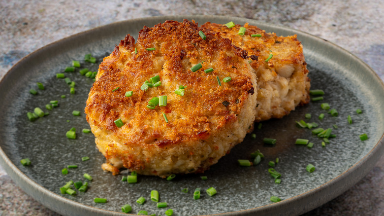 Two crab cakes on a plate garnished with chives