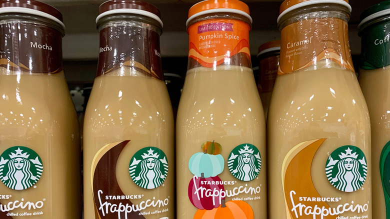 Close up of a variety of Starbucks Frappuccino pre-made bottles in a grocery store, including mocha, pumpkin spice, caramel, and regular coffee flavors.
