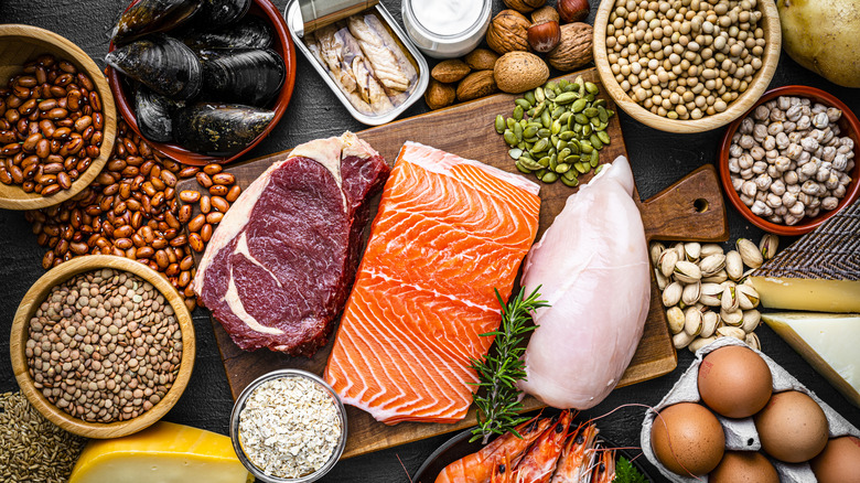 a variety of types of protein laid out on a table, including dried beans, nuts, raw salmon, chicken, and beef