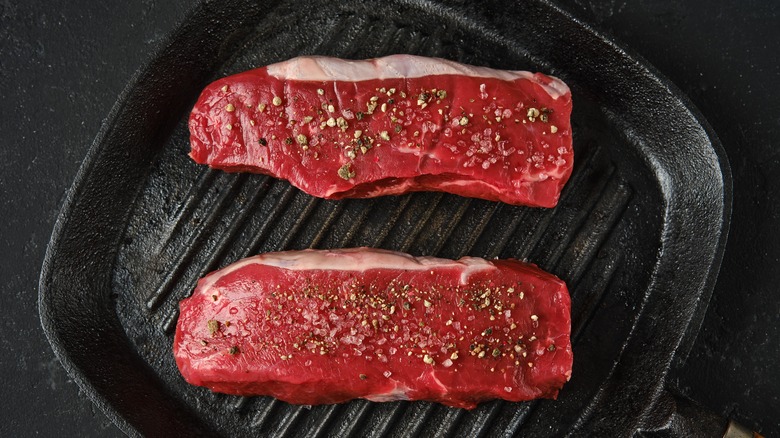 two steaks cooking in a cast iron grill pan