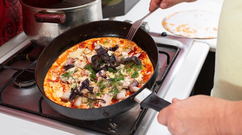 Hands cooking pizza in frying pan