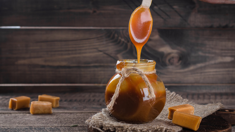 Someone dips a spoon into a small jar of caramel sauce, letting it drip off
