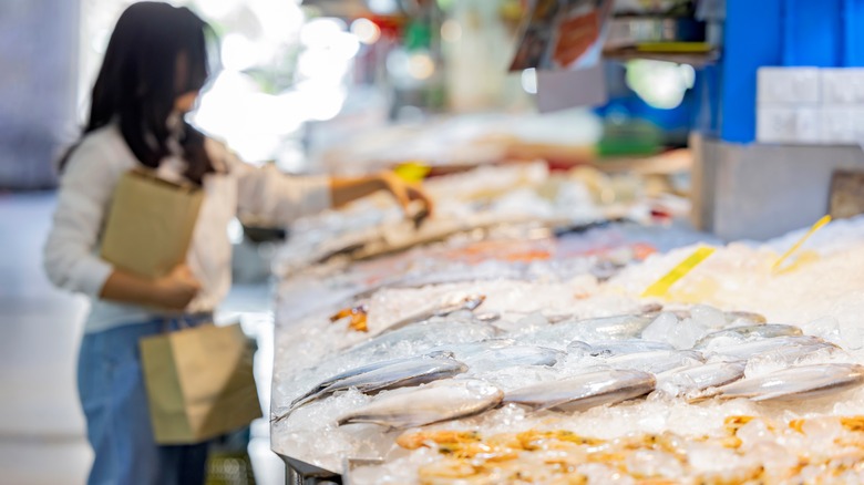 Woman selecting fish from fish counter in grocery store