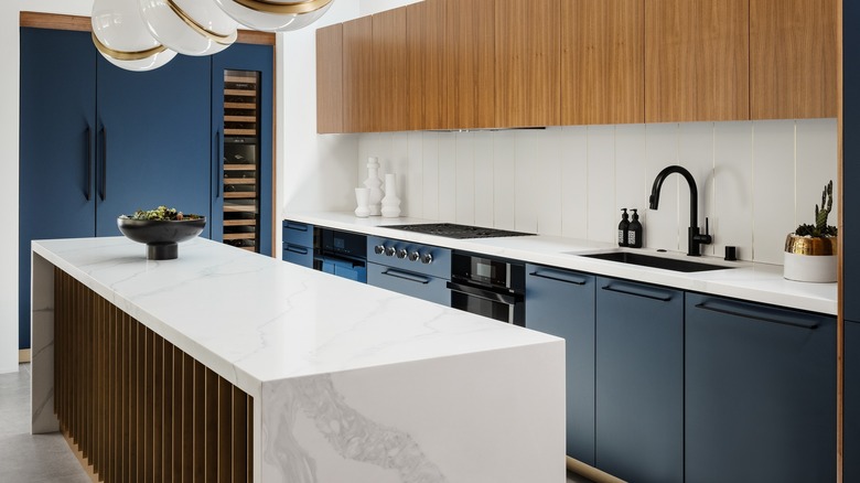 A modern kitchen features a marble countertop island and deep blue cabinetry