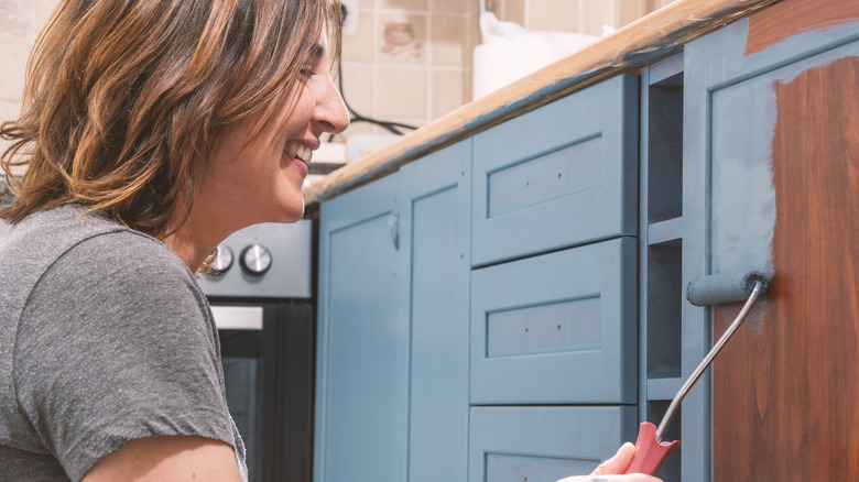 A smiling person paints their kitchen cabinets blue