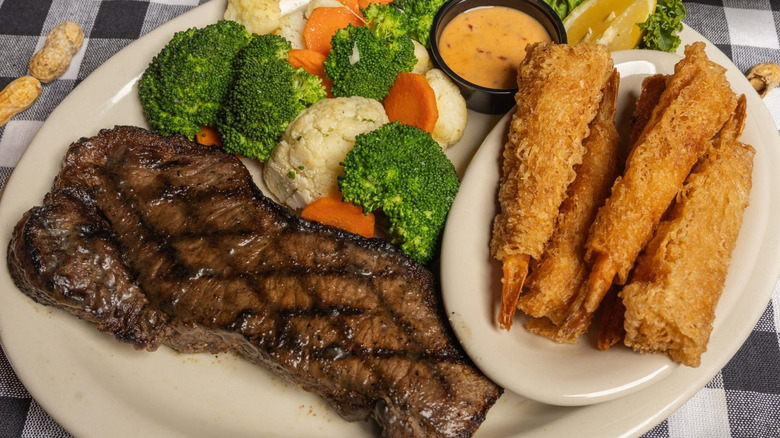 Slab of steak next to broccoli, assorted veggies, and fried shrimp from Cody's Original Roadhouse.