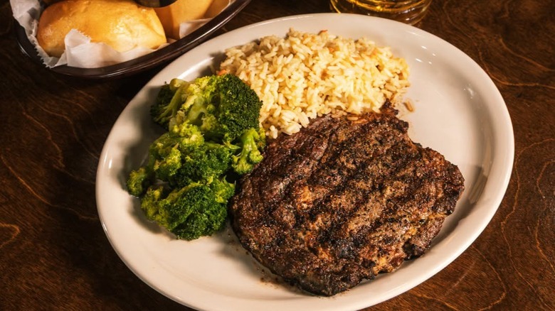 Plate of steak, broccoli, and rice with a basket of bread on the side from Logan's Roadhouse.