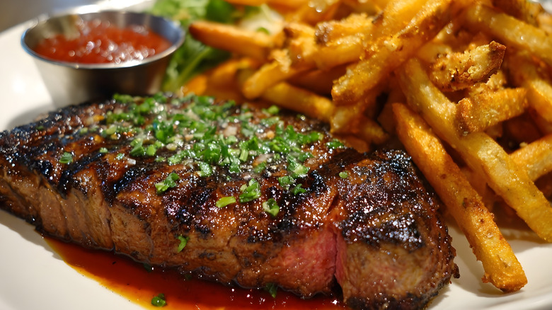 Juicy steak slab with green onion on top next to a side of fries.