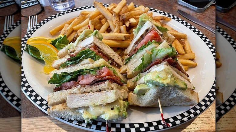 A chicken avocado club and fries sits on a white plate at Black Bear Diner