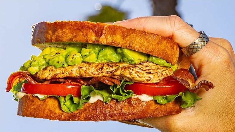 A Habit Burger chicken club is held against a blue sky