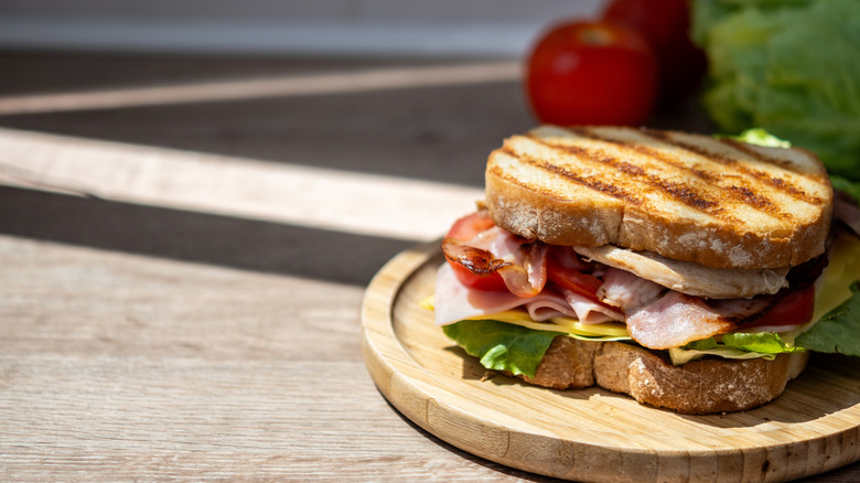 A whole grilled chicken club sandwich sits on a wooden serving board