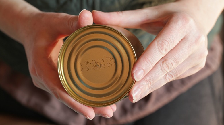 Hands holding canned fish with visible expiration date