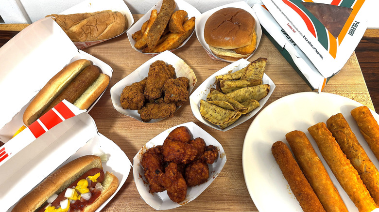 Top view of several different 7-Eleven hot foods including wings, potato wedges, and hot dogs.