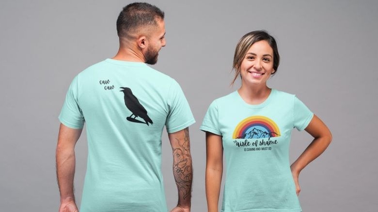 Two people wearing "The aisle of shame is cawing and I must go" Aldi fan T-shirt with a raven "caw caw"-ing on the back