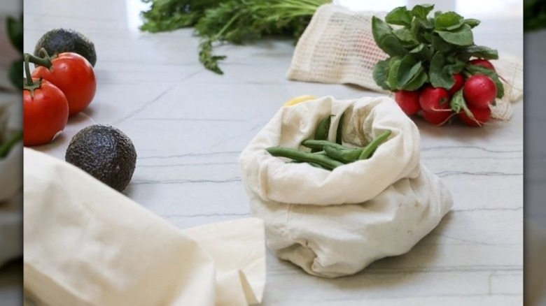 Open off-white muslin bag with stringbeans inside, and other vegetables and bags around it